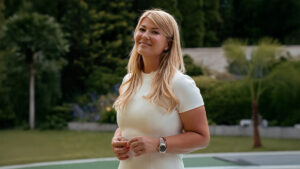 Movik Gabriella ingatlanközvetítő, az Ingatlan Coach iroda alapítója egy fehér ruhában, a háttérben zöld fű és fák látszanak.