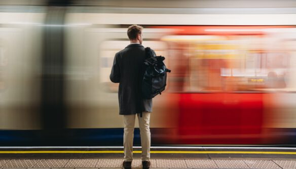 Férfi hátizsákkal vár a peronon, miközben elsuhan mellette egy piros-fehér metró szerelvény.