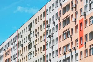 Panelház színes, felújított homlokzattal, számos ablakban és erkélyen klímaberendezésekkel, kék égbolt alatt.