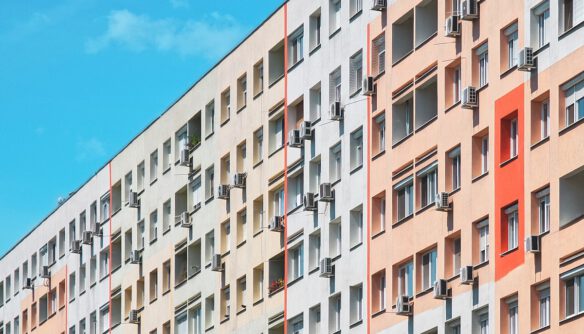 Panelház színes, felújított homlokzattal, számos ablakban és erkélyen klímaberendezésekkel, kék égbolt alatt.